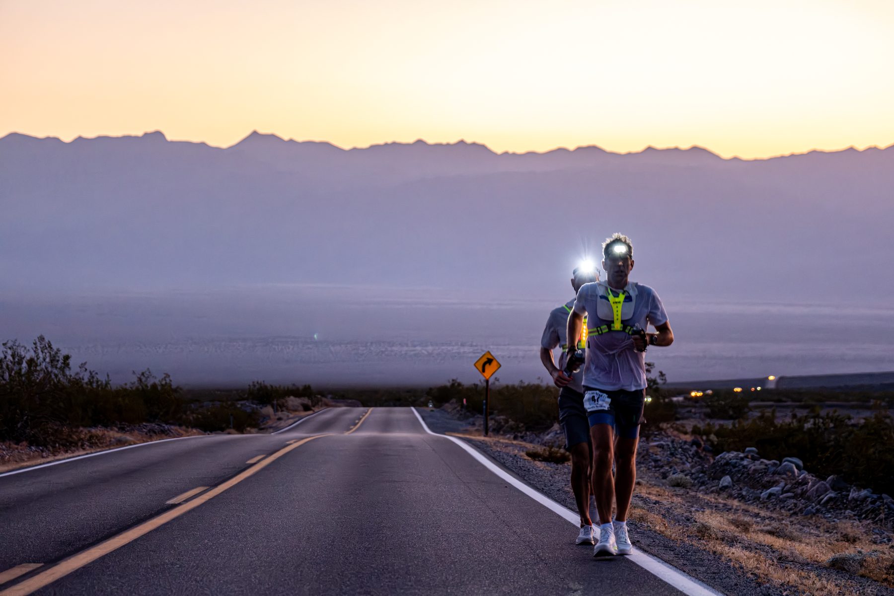 Ben running through Death Valley at dawn during Badwater 135, headtorch lit, mountains behind